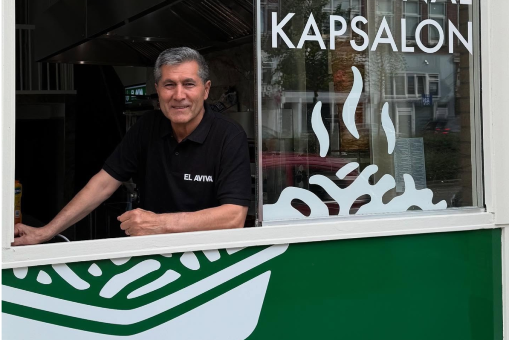 Dervis Bengü voor het raam van shoarmazak El Aviva in Rotterdam, de geboorteplek van de kapsalon.