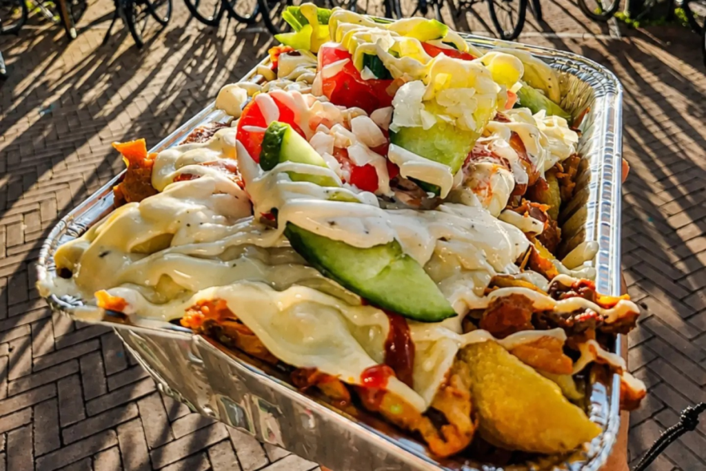 Vers bereide kapsalon in een aluminium bakje met friet, gesmolten kaas, komkommer, tomaat en knoflooksaus op straat