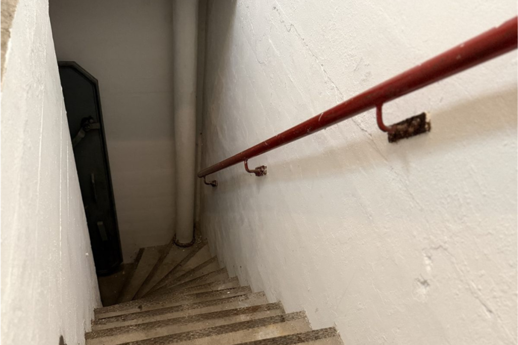 Steile betonnen trap met rode leuning naar de ondergrondse ruimtes van de atoomschuilkelder in Amsterdam.