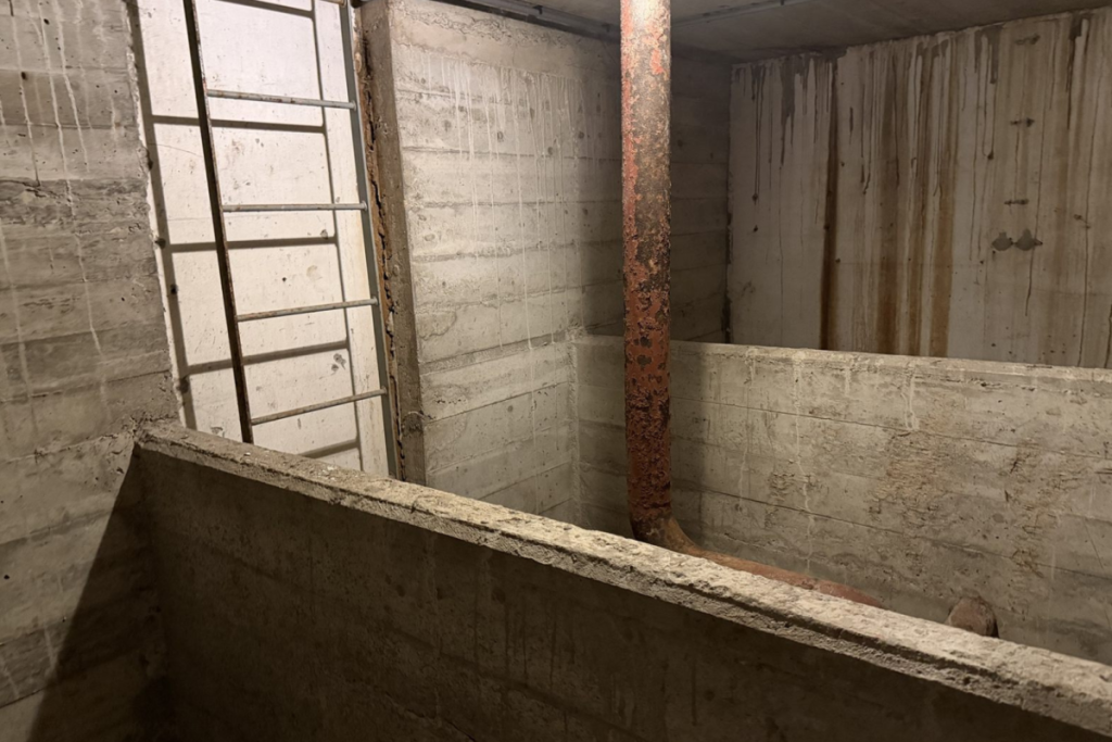 Ondergrondse betonnen pompkelder met massieve wanden, stalen ladder en leidingen van het voormalige rioolgemaal in Amsterdam.