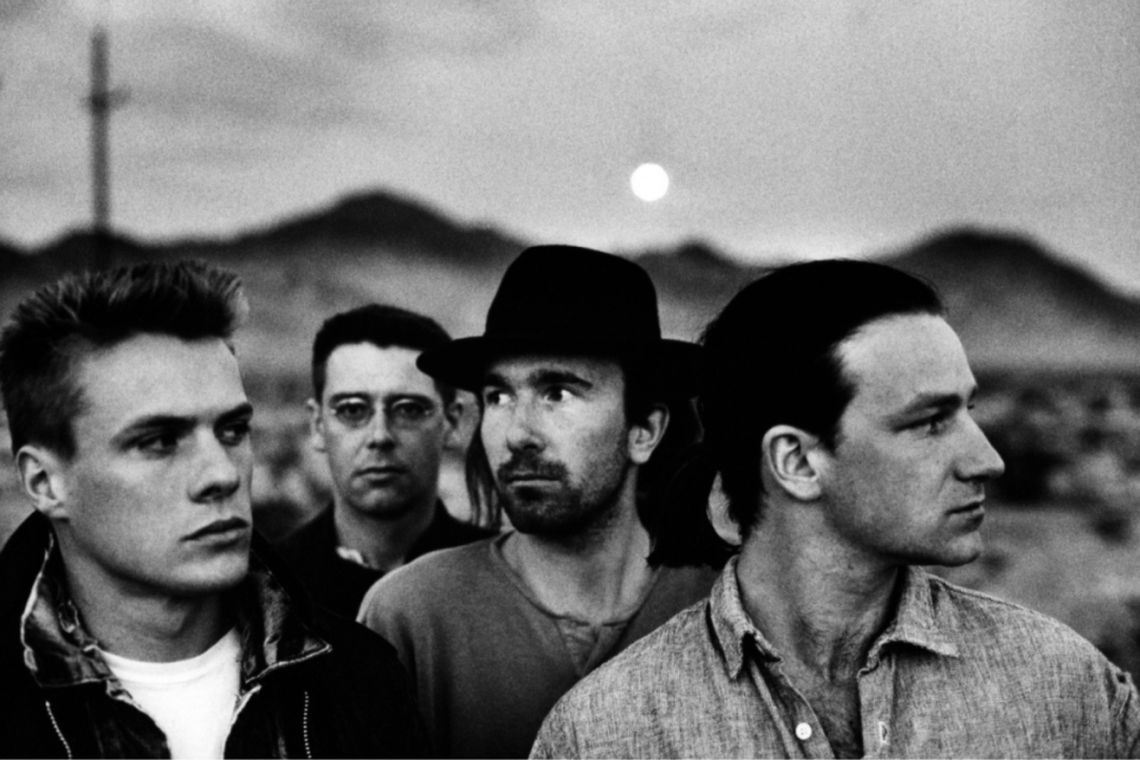 Zwart-wit portret van de Ierse rockband U2 met Bono, The Edge, Larry Mullen Jr. en Adam Clayton in de woestijn tijdens The Joshua Tree-periode