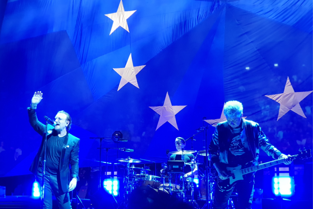 Bono en U2 live op het podium voor een verlicht blauw decor met grote witte sterren