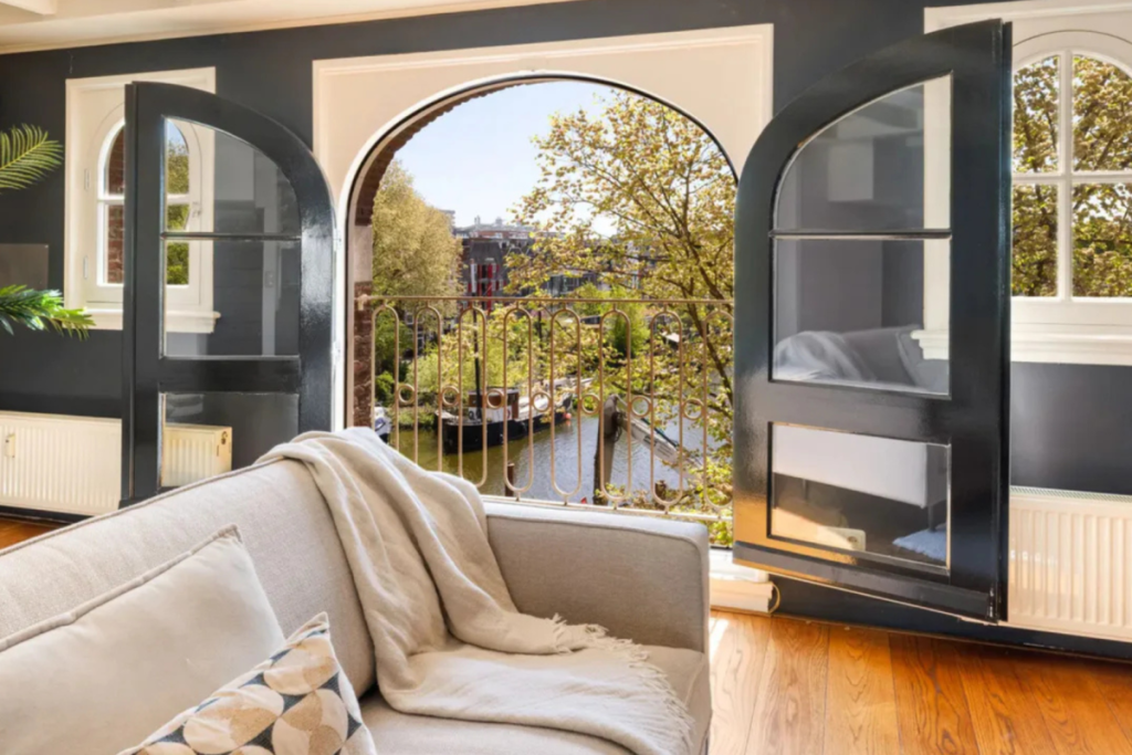 Uitzicht over de Amsterdamse gracht en woonboten vanuit de woonkamer van Jeroen Pauw door openslaande boogdeuren met Frans balkon