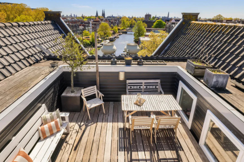 Beschut dakterras op het dak van het pakhuisappartement van Jeroen Pauw met houten vlonders en panoramisch uitzicht over de grachten van Amsterdam