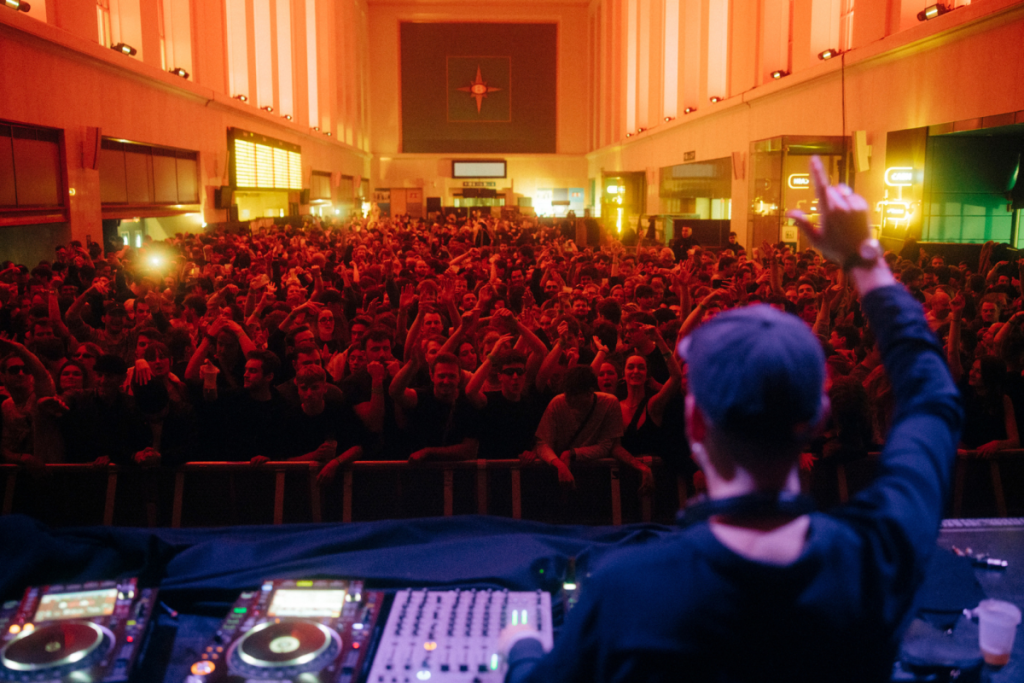 View from the DJ booth over a surging crowd with their hands in the air during Listen Festival in Brussels