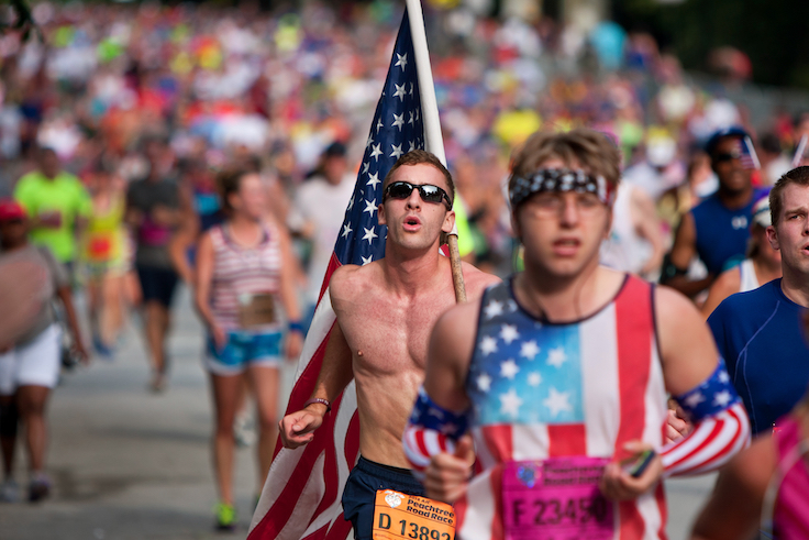 ATLANTA, GA - JULY 4: A young man carries a large American flag on his shoulder as he runs among thousands of people nearing the finish line of the Peachtree Road Race on July 4, 2014 in Atlanta, GA.