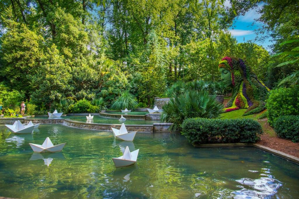 a stunning summer landscape in the garden with The Earth Goddess covered in colorful flowers surrounded by lush green trees, grass and plants with blue sky at Atlanta Botanical Garden in Atlanta
