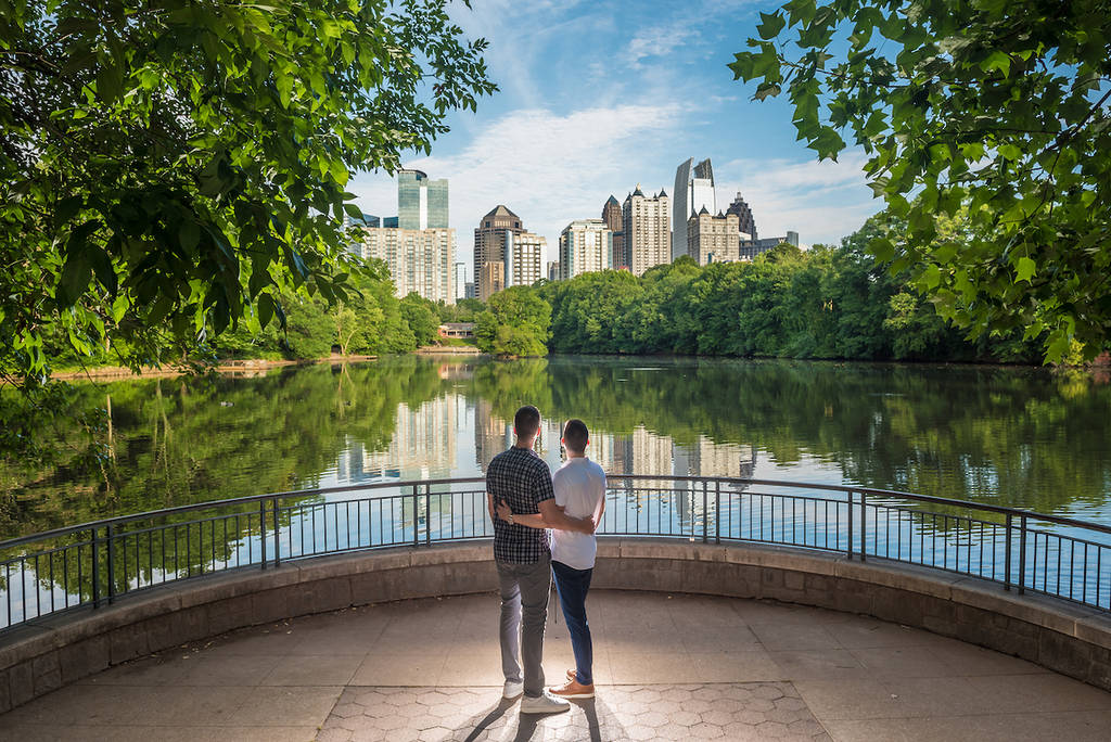 Atlanta, GA, USA - 06-04-21: Pair of two gay men posing in Piedmont Park looking at the city skyline with lake in background