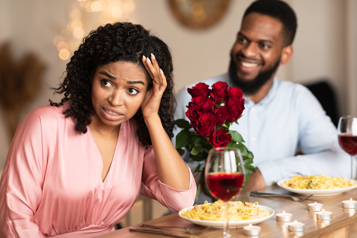 Bad First Impression And Blind Date Concept. Dissatisfied shocked black woman rejecting excited emotional obsessed man who giving her flowers, young couple sitting at table in cafe