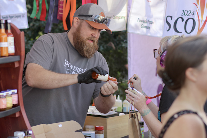 man serving hot sauce on a sample plate to a woman