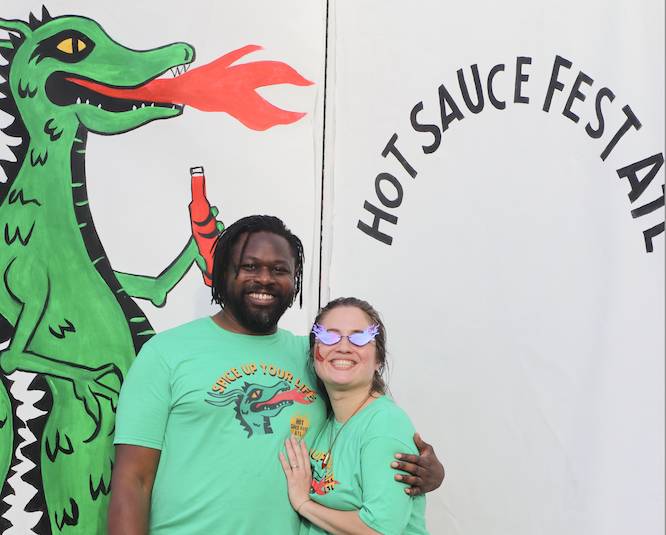 couple posing with a painting of a green dragon at a hot sauce festival