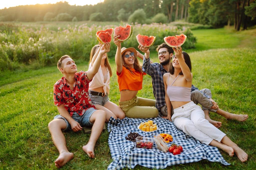 Group of friends having fun eating watermelon on the picnic outdoors. Foods, travel, nature and vacations concept