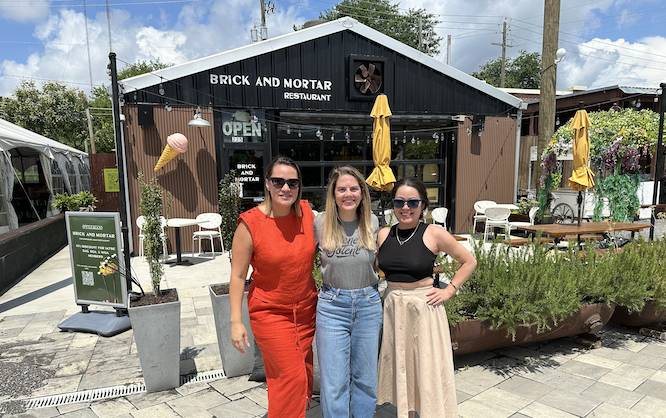 outside of a building with plants and a cute patio and three women standing in front of it