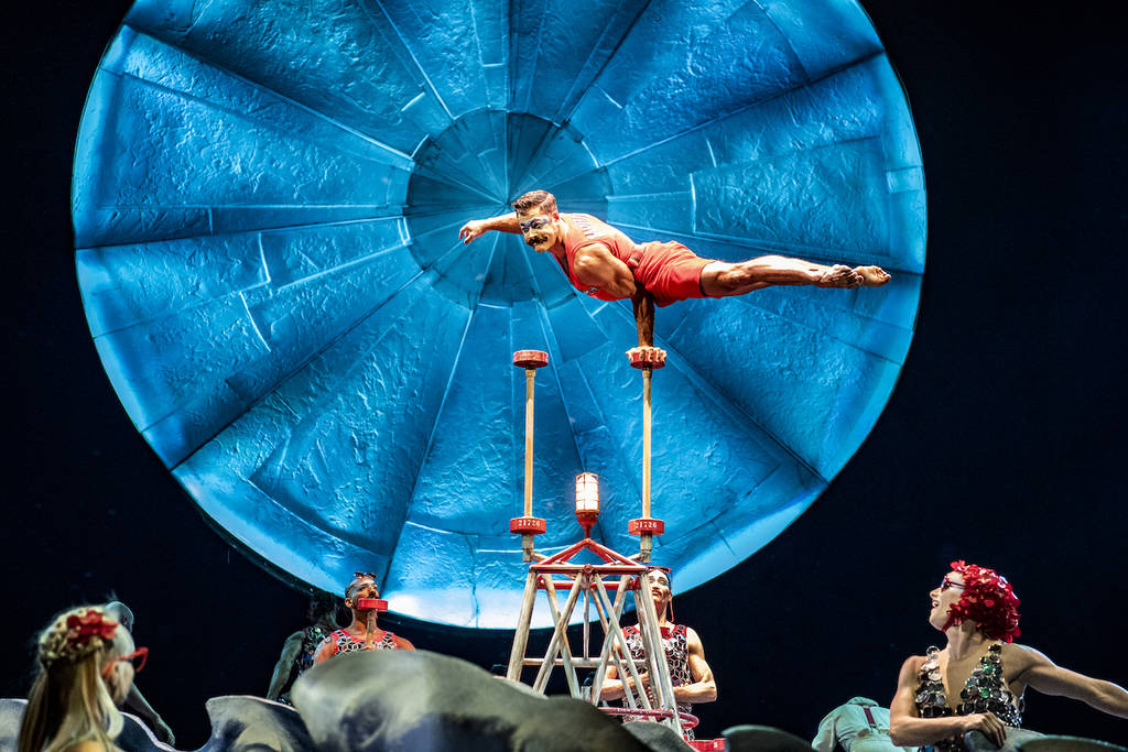 male acrobat holds his whole body weight up with just a single hand while balancing on a pike