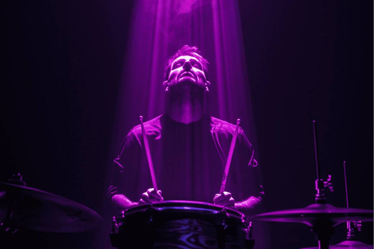 man is illuminated by purple light whilst he plays the drums