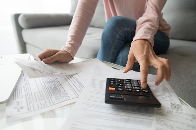 Woman renter holding paper bills using calculator for business financial accounting calculate money bank loan rent payments manage expenses finances taxes doing paperwork concept, close up view