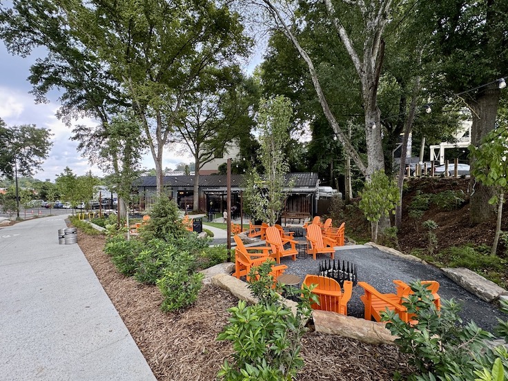 a new patio location at a local brewery surrounded by green grass and a blacktop pavement and bright orange chairs
