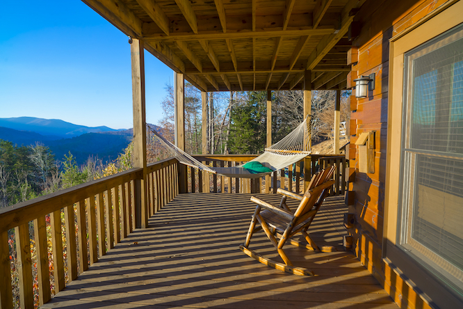 Cabin vacation. Hammock and rocking chair on terrace at cabin. View of blue mountains and blue sky. Rest and relax in the mountains at fall. Wooden house at Blue Ridge mountains, GA. Cabin getaway.