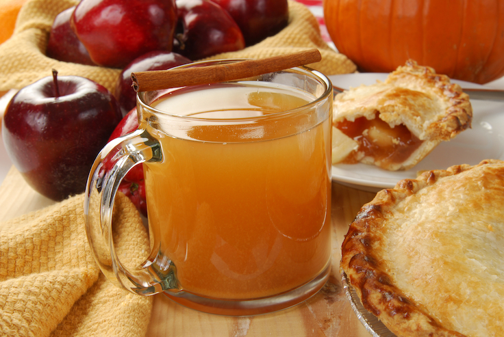 A cup of hot apple cider by an apple pie