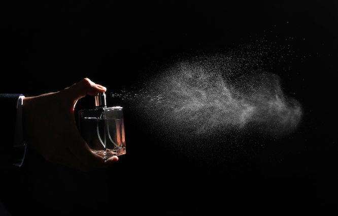 Man spraying luxury perfume on black background, closeup