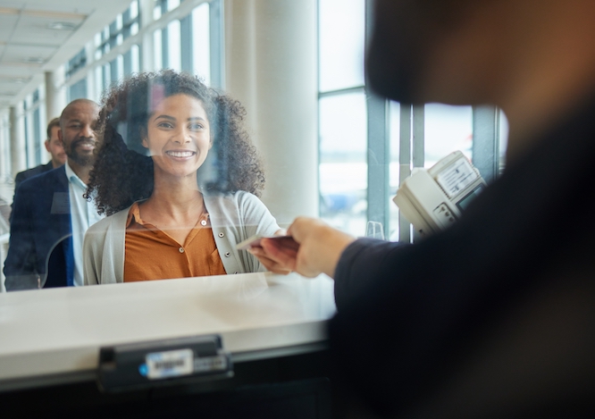Black woman, ticket check and airport counter with a paper for travel or box office service. Happy customer person at consultant booth window for passport, work booking and buying pass at seller