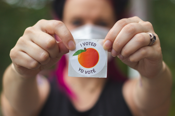 Lawrenceville, Georgia / United States - October 29 2020: A Georgia voter wearing a mask holds up her "I Voted" sticker after voting in the 2020 United States Presidential election