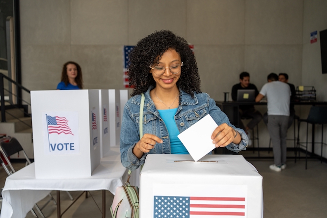 portrait of a young african american woman voting in the us election, placing vote ballot in the polling box, vote in America. Concept of choice, democracy and freedom