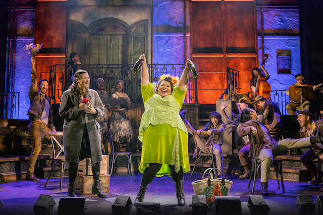 woman in a green dress standing on a stage with workers surrounding her