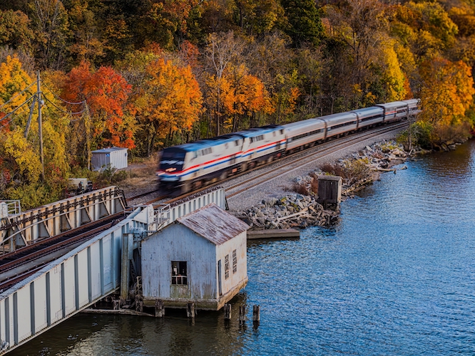 New Hamburg, NY United States - October 25, 2024: An aerial view of Amtrak train passing by, taken from over the Hudson River on a sunny day in autumn.