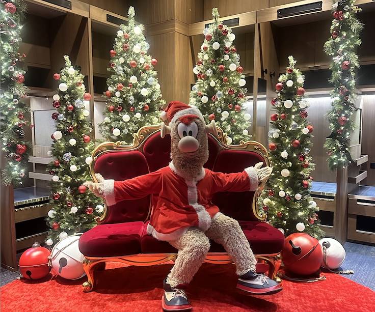 Braves mascot, BLOOPER, wearing Christmas attire, surrounded by Christmas trees