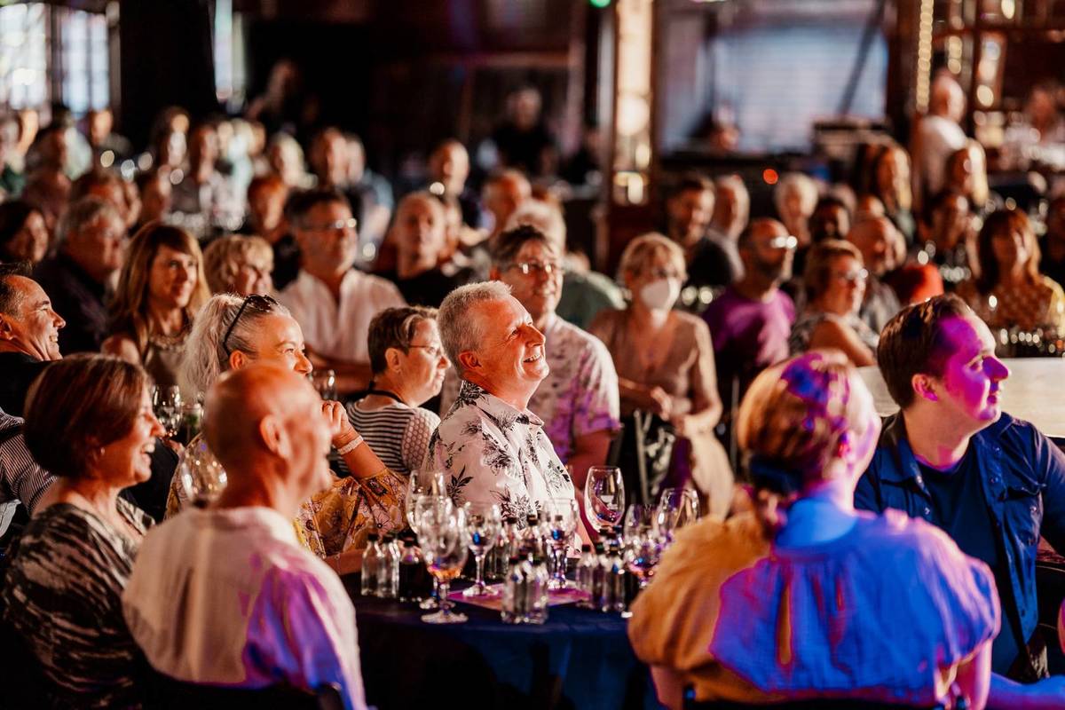 Audience members around tables watching the comedian on stage