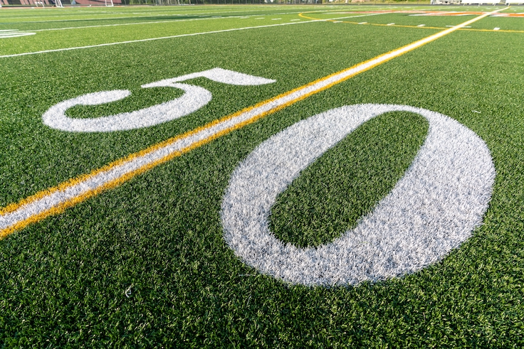 Synthetic turf football field fifty, 50, yard line in white.