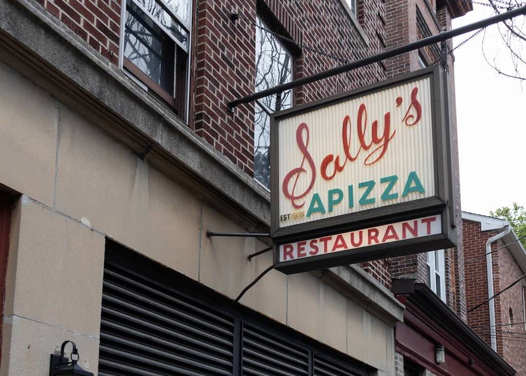 an old-timey looking pizzeria with a sign that says 'Sally's Apizza' on it