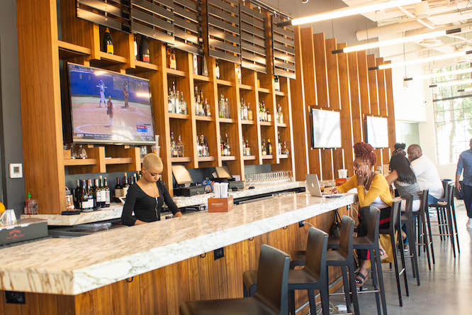 una camarera con grandes televisores deportivos detrás de ella.