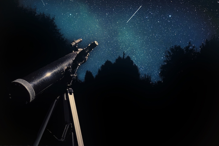 A black telescope on a tripod points up to a dark blue night sky filled with stars. The image gives the impression of observing space