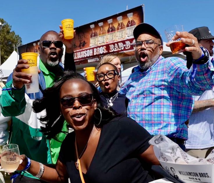 Una familia posando con bebidas y comida en un festival gastronómico al aire libre.