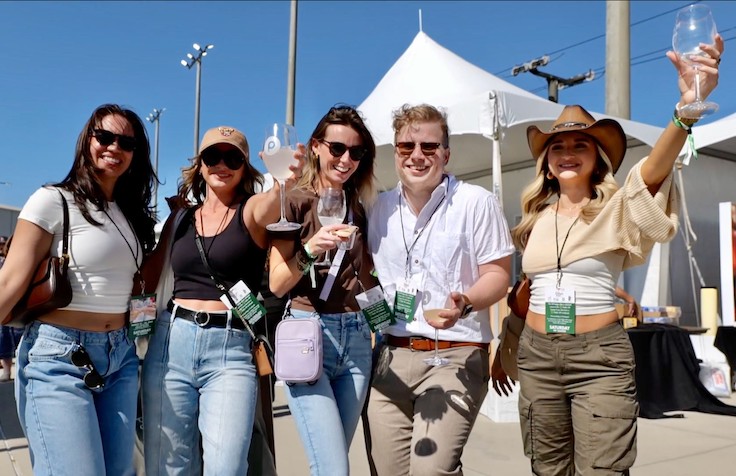 Una familia posando con bebidas y comida en un festival gastronómico al aire libre.