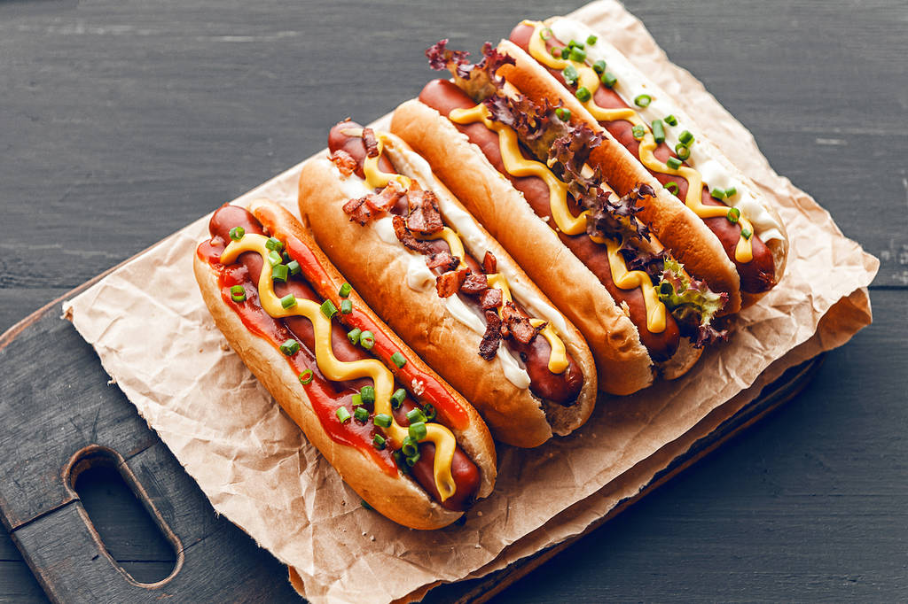 Perritos calientes a la barbacoa con mostaza americana amarilla, sobre un fondo de madera oscura