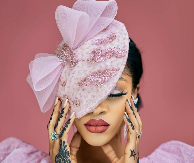 a beautiful Black woman with a pink fascinator hat on and hand tattoos 