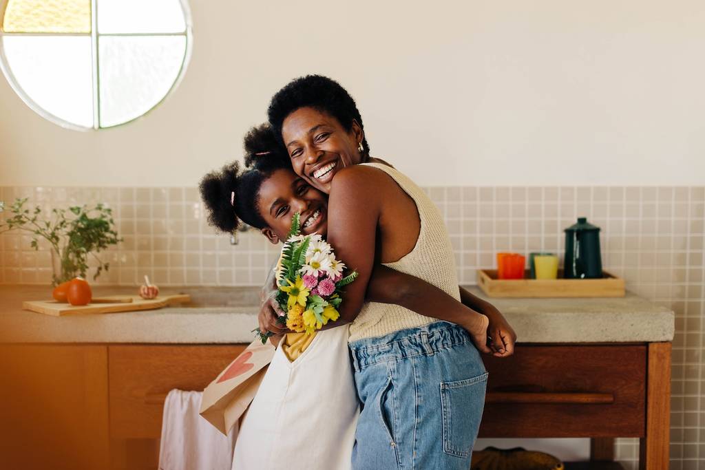 Daughter surprises her mom with a heartfelt gift of flowers in the kitchen, sharing a loving moment and bringing happiness to their home. Perfect for Mother's Day or any special occasion.