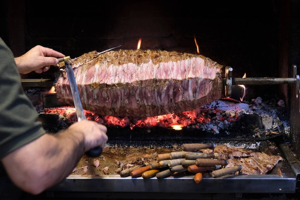 Turkish cag kebab or yatik döner. Traditional Turkish roasted meat. Cag Kebab cooks at the wood fire on a horizontal rotisserie. Cutting and serving the roasted part of the meat.