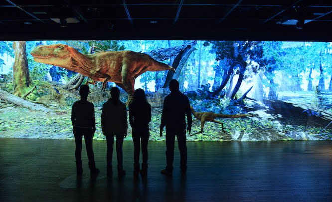 people standing in a room with a Dino movie playing