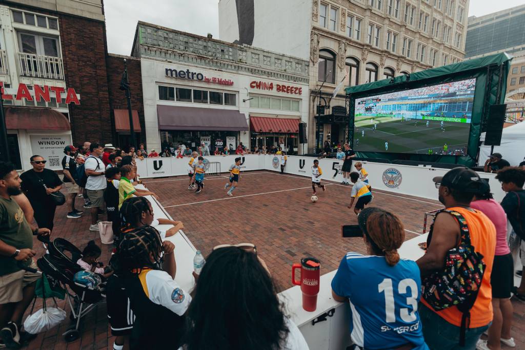 niños jugando al fútbol delante de una pantalla en la que se ve el Mundial