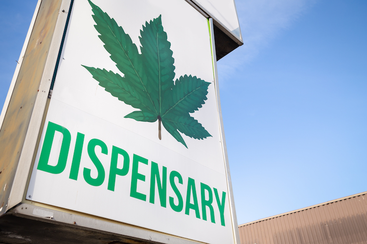 Un cartel de un dispensario de cannabis con una gran hoja de marihuana.
