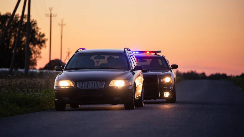 Un conductor que va a exceso de velocidad es detenido por un coche patrulla de la policía. Plano general de los dos coches parados en una carretera que atraviesa un campo abierto. Un conductor ebrio es detenido por agentes profesionales
