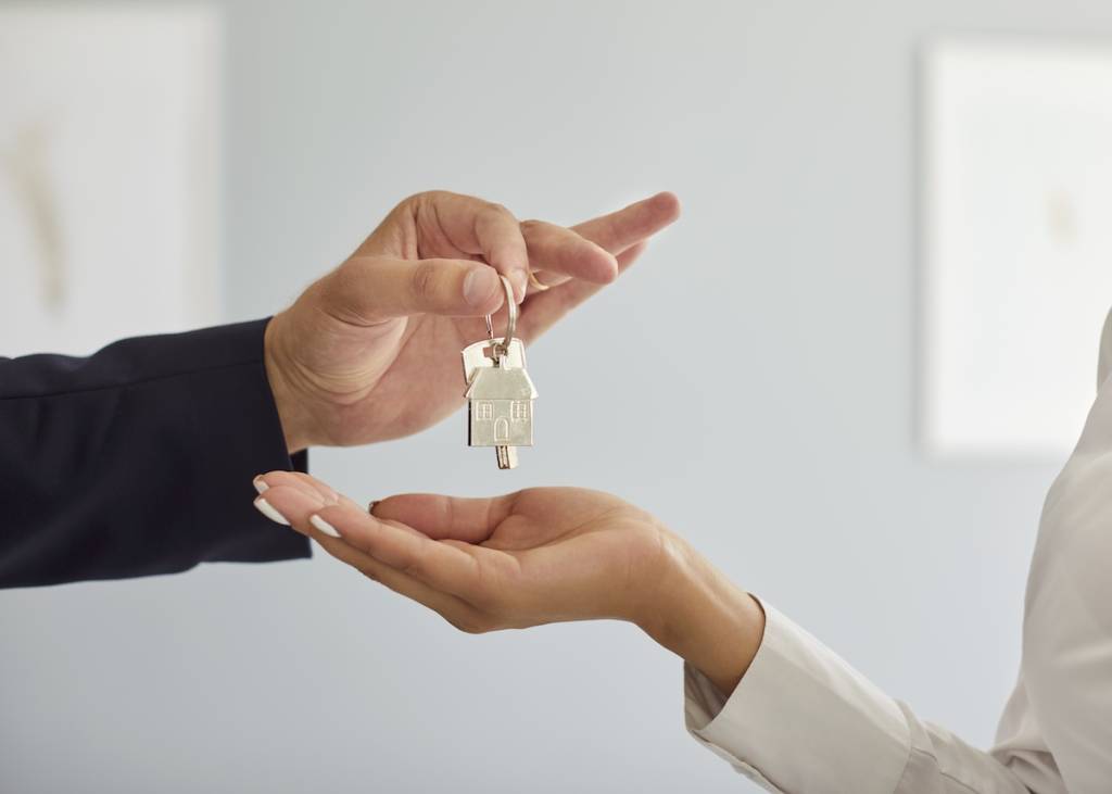 Agente inmobiliario profesional entregando las llaves de la nueva vivienda a la compradora. Primer plano recortado de la mano de un agente inmobiliario entregando las llaves de un nuevo piso a una joven clienta. Concepto de compra o alquiler de una vivienda.