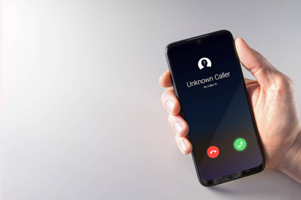 Mano de un hombre sosteniendo un smartphone en cuya pantalla aparece una llamada de un número desconocido. Conceptos de privacidad, fraude, ciberdelincuencia y espionaje