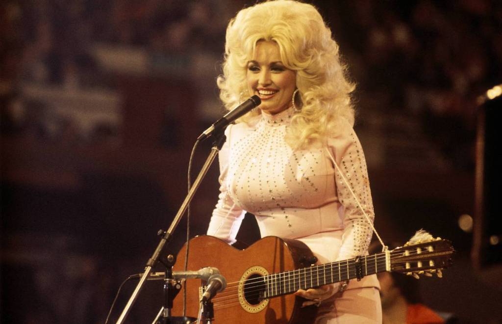 UNITED KINGDOM: American singer, songwriter and actress Dolly Parton, performs with a guitar, 1976. (Photo by David Redfern/Redferns)