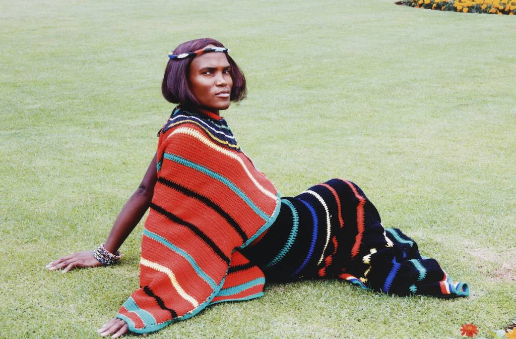 a woman sitting on a grass field in traditional African attire