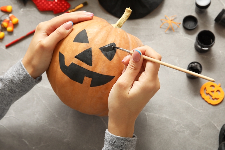Mujer pintando una calabaza de Halloween en una mesa gris de estilo grunge